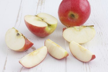 Pink lady apples cut on a white rustic wood table.