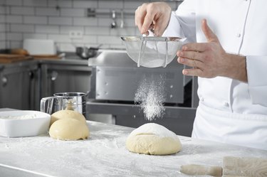 Chef sifting flour over a ball of dough