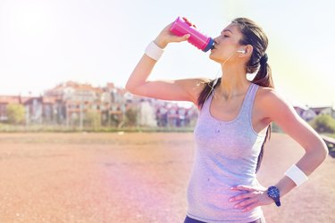 Young sportswoman drinking water after running
