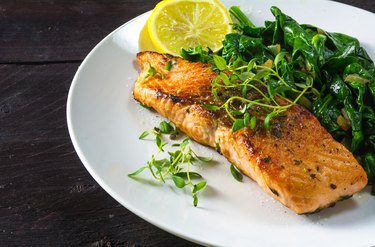 grilled salmon withspinach on a white plate, dark wooden table