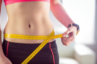 Slim woman measuring waist with tape measure