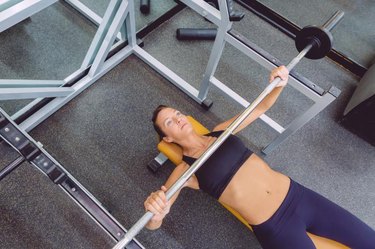 Beautiful woman doing exercises with barbell on a bench press training in a fitness center