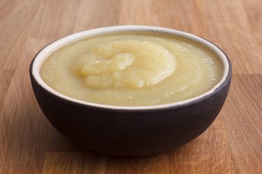 Apple sauce in rustic brown dish on dark wood.