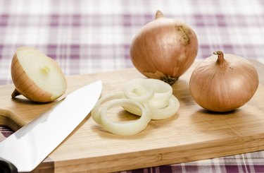 Onions and onion rings on cutting board with knife.