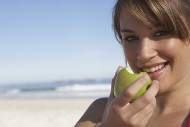 Young woman holding apple, outdoors, smiling, close-up, portrait