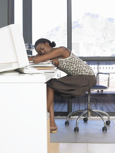 Young woman leaning on pile of files on desk, sleeping