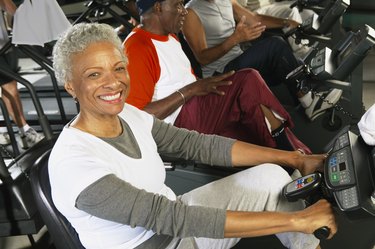 Senior woman using cycling machine in gym, smiling, portrait