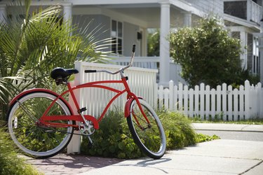 Red beach cruiser bicycle propped against fence in front of house.