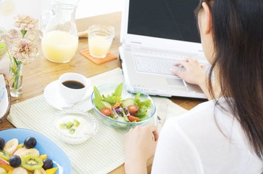 Woman having breakfast while using her laptop