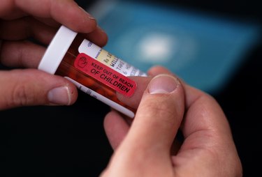 Person holding plastic bottle filled with pills, close-up