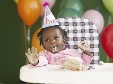 African baby in high chair wearing party hat and eating cake