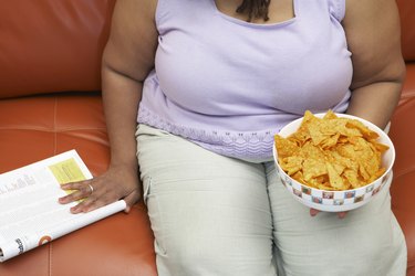 Woman sitting on couch with magazine and crisps, mid section