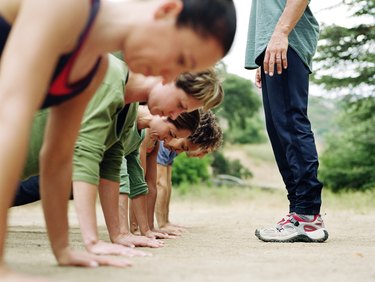 Man standing over group of people doing pushups, side view