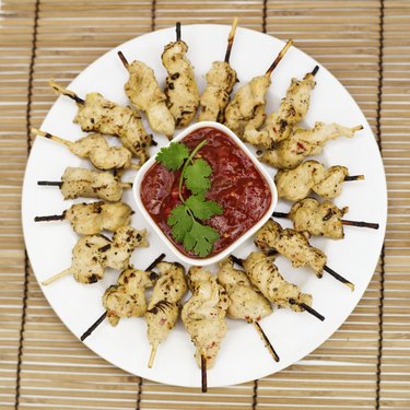 Elevated view of a plate of chicken kebabs on skewers with sauce in the center of plate