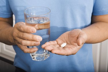 a close up photo of a person wearing a blue t-shirt holding a vitamin supplement in one hand and a glass of water in the other