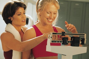 Woman standing on a scale as trainer helps weigh her