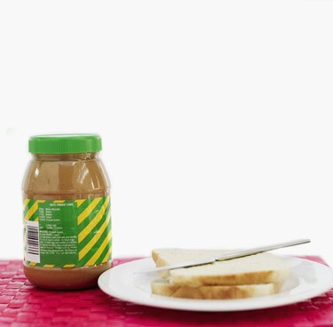 A jar of peanut butter next to a plate with bread and a butter knife