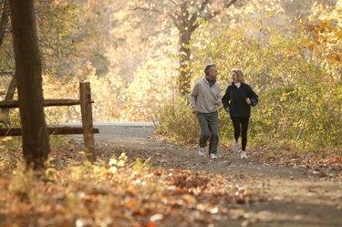 Couple jogging down path through fall leaves