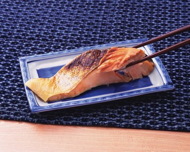 Chopsticks holding a piece of broiled sliced salmon on plate, high angle view