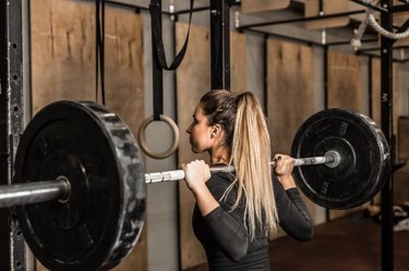 Closeup young and fit female athlete performed squats in the gym.Beautiful blonde girl during workout in gym with barbell on her shoulders.