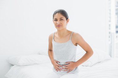 Casual woman with stomach pain sitting in bed