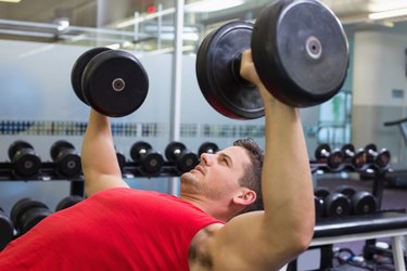 Bodybuilder lying on bench lifting dumbbells