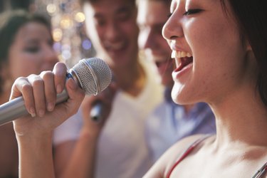 Close-up of young, healthy vocalist holding a microphone and singing karaoke with friends.