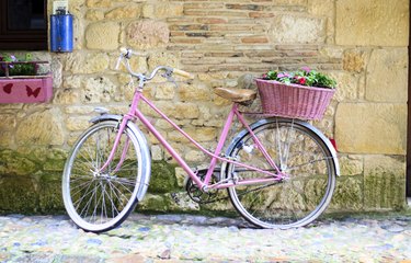 Pink bike that has been spray painted with bike paint with basket of flowers on the back near a stone wall
