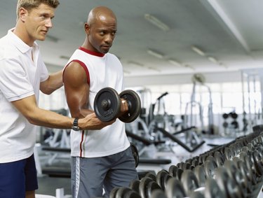 Coach helping a mid adult man exercise with dumbbells