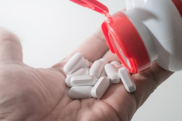close-up of open medication bottle with tablets being poured into hand