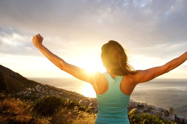 Portrait of woman from behind stretching out her arms in front of sunrise