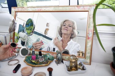 Mirror reflection of senior woman spraying perfume on herself at home