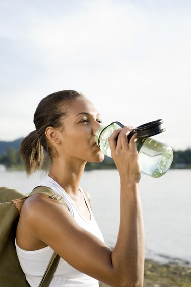 Athletic, thirsty hiker in sportswear drinking from water bottle and hiking in remote area