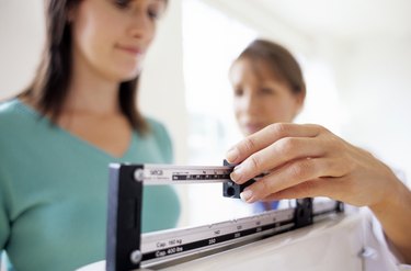 Doctor adjusting balance on weighing scale while patient checking weight