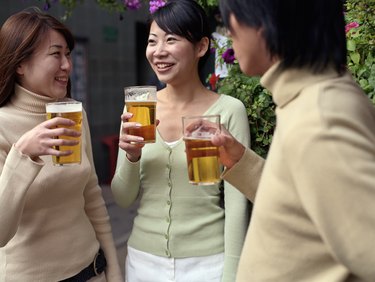 Two young women and young man holding pints of beer outside pub