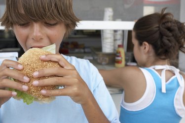 Boy (9-11) eating hamburger, girl (12) queuing at vendor's window