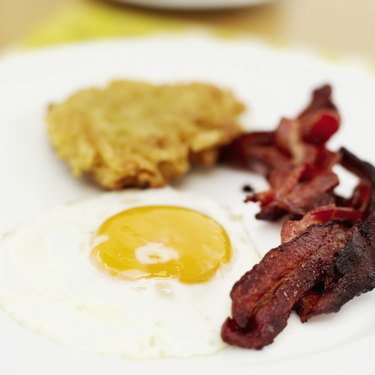 Close-up of a fried egg with bacon and hash browns on a plate