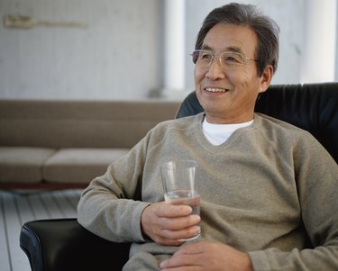 Senior man sitting on armchair holding glass of water, smiling