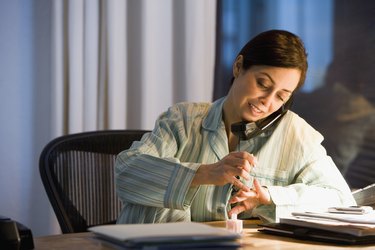 Hispanic businesswoman painting fingernails at desk