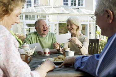 Two senior couples looking at photographs around garden table, smiling
