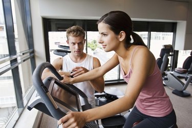 Man watching woman on exercise bike at gym