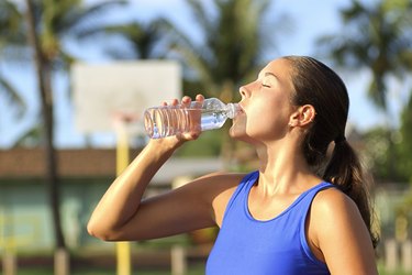 Side view of a woman drinking water from a bottle after exercising