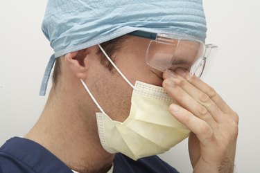 Male doctor wearing surgical mask and cap, rubbing eyes, side view