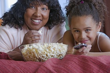 Two people laying on the couch eating popcorn