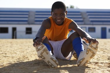 Portrait of boy (10-11) sitting on playing field, stretching