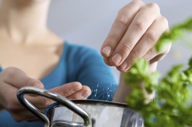 close up of hands sprinkling a dash of salt into a pot of water