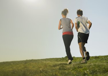 Man and woman jogging on grass, rear view