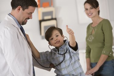 Boy giving thumbs-up while using stethoscope on doctor