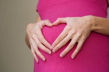 Woman holding hands in heart on pregnant stomach