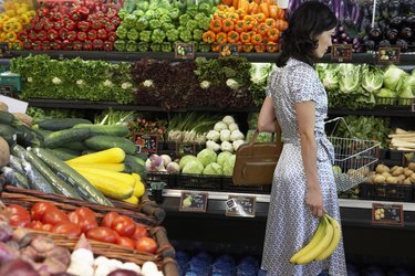 Woman holding bananas in produce aisle of supermarket, side view